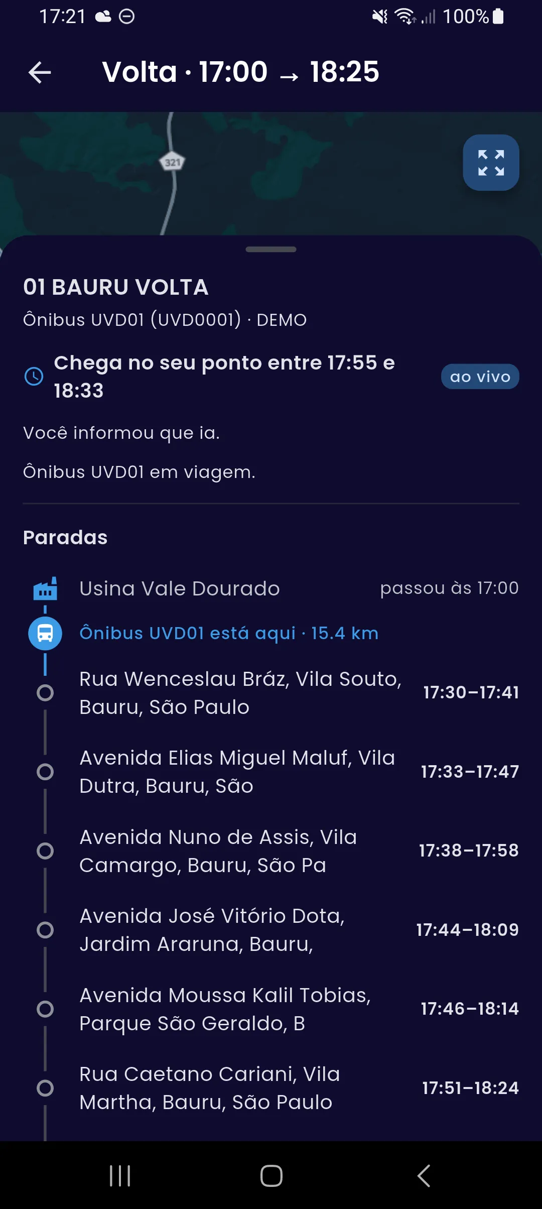 Detalhe da volta em andamento no aplicativo: a janela de chegada no ponto do passageiro, ao vivo, a confirmação de que ele informou que ia e a lista de paradas com o ônibus posicionado entre a saída e a primeira parada, a quilometragem percorrida e a janela de passagem prevista em cada ponto.